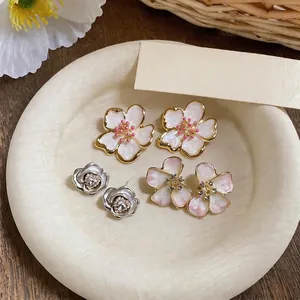 Elegant French-style enamel floral stud earrings displayed on a textured beige plate.