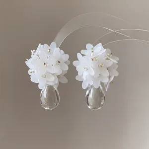 Detail view of white flower cluster earrings with clear water-drop shaped resin pendants