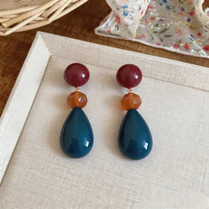 Detailed macro view of colorful resin water drop earrings in a warm lifestyle setting.