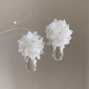 Macro detail of elegant white floral cluster earrings with clear teardrop pendants