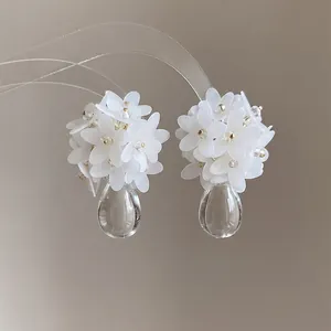 Macro detail of elegant white floral cluster earrings featuring clear teardrop resin pendants