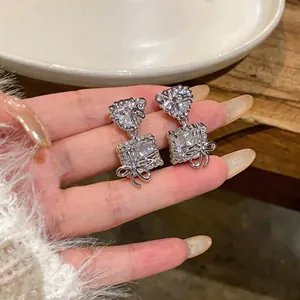 Detailed macro view of elegant silver heart and square bow earrings with clear zircons.