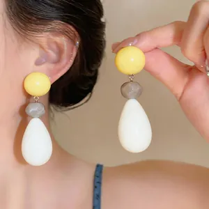 Close-up of vibrant resin teardrop earrings in yellow, grey, and white on a model