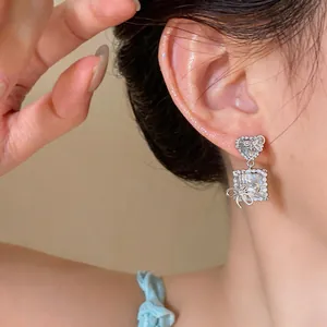 Close-up detail view of heart and square zircon earrings with delicate silver bows