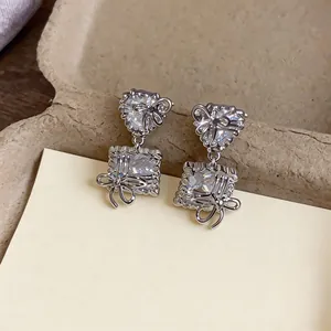 Close-up of elegant silver bow drop earrings with heart and square zircon stones.