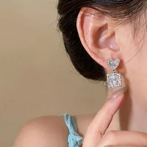 Close-up detail showing elegant silver bow earrings with heart and square zircon charms on ear