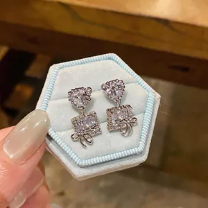 Close-up view of heart and square shaped zircon earrings with bows in a blue jewelry box