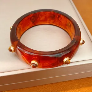 Vista dettagliata di un bracciale in resina con effetto marmo ambra e rivetti dorati lucidi