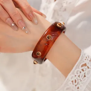 Dettaglio di un bracciale rigido in resina ambrata vintage con borchie dorate.