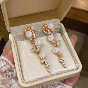 Dettaglio ravvicinato di eleganti orecchini a spiga dorati con perle e zirconi bianchi