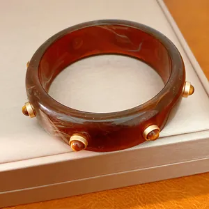 Primo piano di un bracciale in resina marmorizzata con borchie dorate su un portagioie neutro