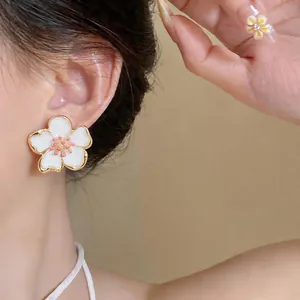 Elegant white drip oil flower stud earrings with gold-tone edges worn on a model's ear
