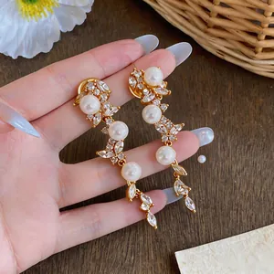 Dettaglio di eleganti orecchini a spiga dorati con perle e zirconi taglio marquise
