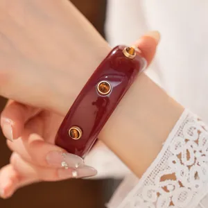 Dettaglio ravvicinato di un bracciale vintage in resina rossa con rivetti dorati