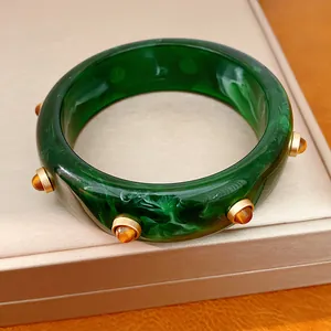 Primo piano dettagliato che mostra la trama marmorizzata verde e i rivetti dorati del bracciale.