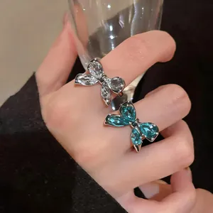 Vista de detalle de elegantes anillos de lazo con circonitas azules y transparentes en una mano.