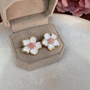 Detailed view of elegant white enamel flower stud earrings with gold trim in a beige box