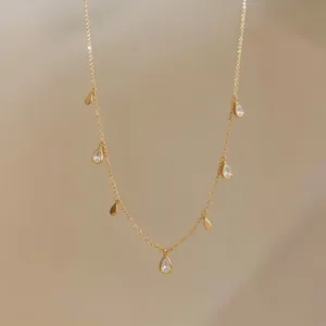 Dettaglio di una collana dorata minimalista con pendenti a goccia in metallo e zirconi lucidi