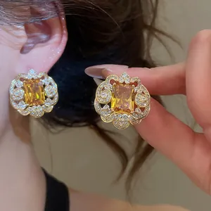 Macro detail of luxury square yellow zircon stud earrings with gold floral lace border