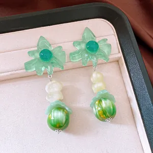 Detailed close-up view of green flower pendant earrings with marbled beads on a jewelry tray