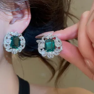 Close-up of emerald green square zircon earrings with sparkling floral border and luxury feel