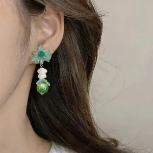 Detail shot of summer style flower dangle earring featuring a green bead and cute white bear.