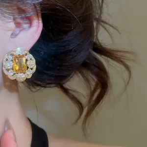 Detail of a luxury gold-toned flower stud earring with a large square yellow zircon gem.