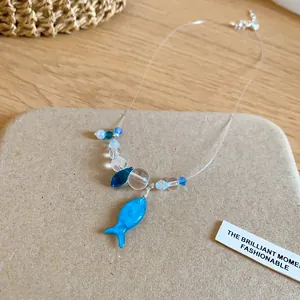 Detailed close-up of a blue resin fish pendant on a clear beaded necklace for women.
