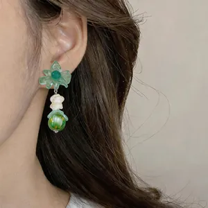 Detail view of green flower dangle earrings worn on an ear, showing delicate textures
