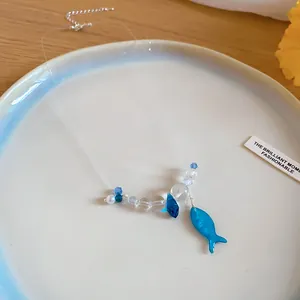 Detail view of blue resin fish pendant with clear beads on a transparent choker string