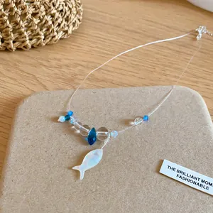 Macro view of blue and white resin beads with a small fish charm on a delicate wire necklace