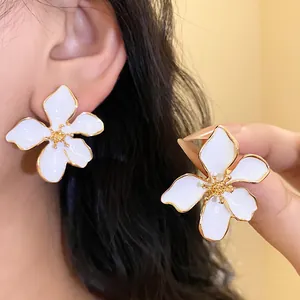 Close-up view of elegant white enamel flower stud earrings with gold trim on a model