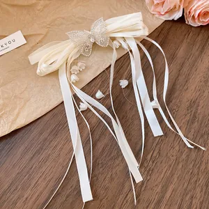 Close-up of elegant cream satin bow hair clip with crystal butterfly and lily pendants