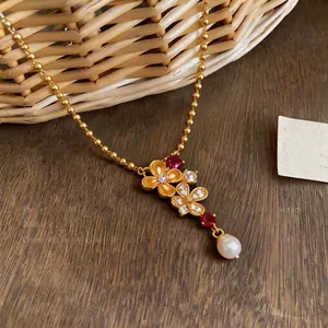 Elegante 24k vergoldete Blumenhalskette mit rotem Zirkon und Perle auf einem Holztisch