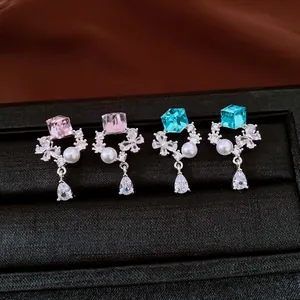 Close-up of zircon teardrop pearl earrings with pink and blue cube crystals in a box