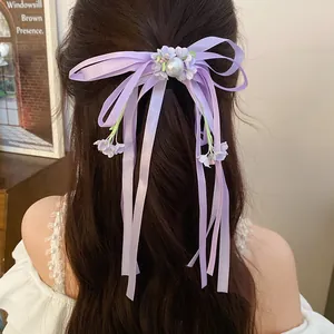 Detailed view of a purple ribbon bow hair clip with pearl and floral tassel on hair.