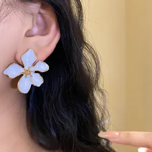 Close-up detail view of elegant white enamel flower stud earring with gold edges on ear.