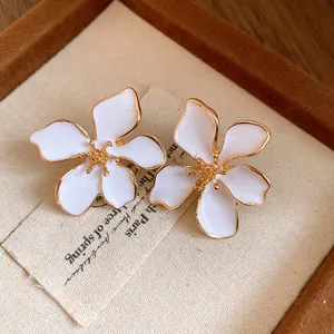 Close-up of elegant white enamel flower stud earrings with gold-tone trim and details