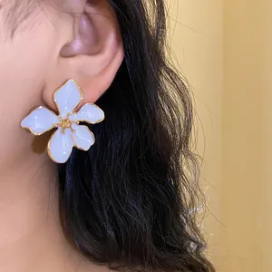 Close-up detail of white enamel flower stud earring with golden trim worn on ear