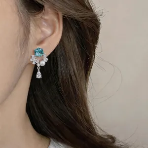 Close-up of elegant blue zircon and pearl earrings with silver needles on earlobe