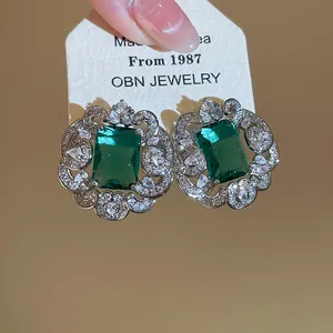 Close-up of emerald green square zircon stud earrings with ornate silver lace border