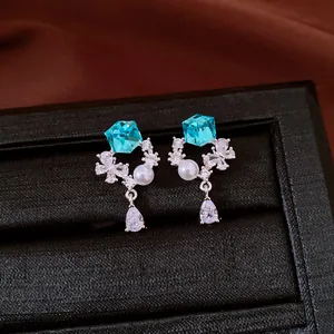 Close-up of elegant stud earrings featuring blue crystal cubes and pearl accents