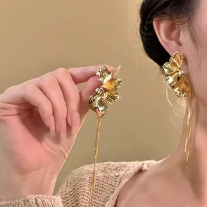 Detailed macro shot of elegant golden flower tassel earrings worn on ear and held by hand