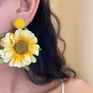 Handmade sunflower raffia fabric drop earrings worn on ear showing delicate petals