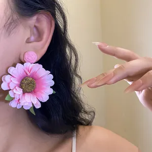 Detailed view of large pink fabric flower dangle earrings with woven raffia stud.