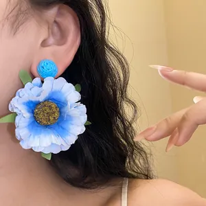 Macro shot of a large blue raffia flower stud earring showing detailed fabric petals.