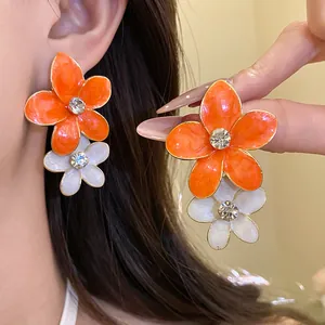 Close-up of vibrant orange and white flower drop earrings with sparkling crystal centers