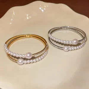 Close-up detail of double-layer pearl and rhinestone bracelets in gold and silver finish