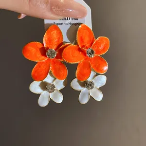 Close-up of enamel flower earrings with orange and white petals and rhinestones