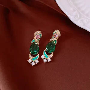 Close-up of vintage gold earrings with emerald green teardrop and pink zircons